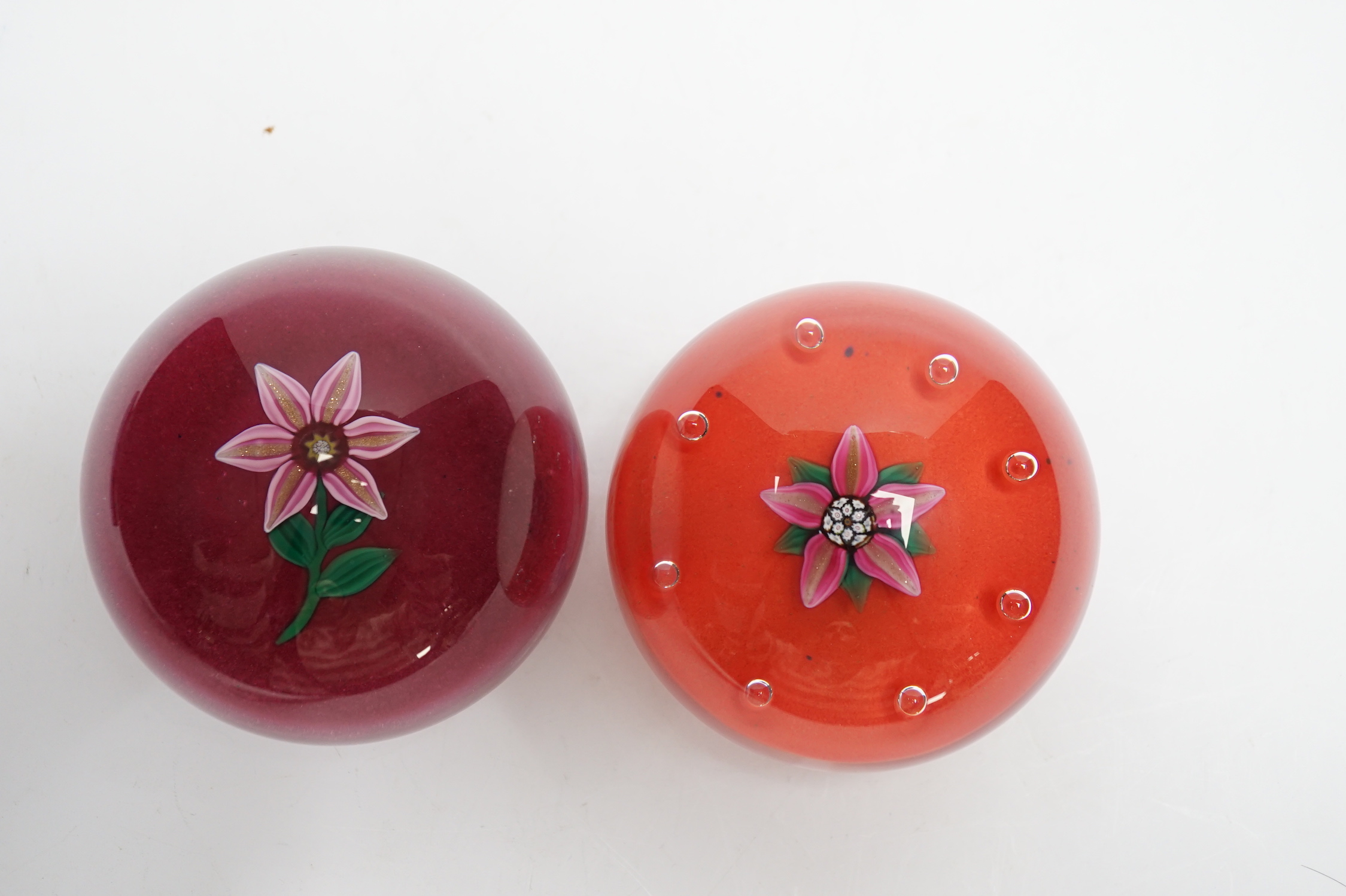 Two Paul Ysart glass ‘flower specimen’ paperweights, both Harland period, the first with a pink and aventurine flower with green stem on a raspberry ground, H cane to base, PY label, 7cm, The second with a pink and adven